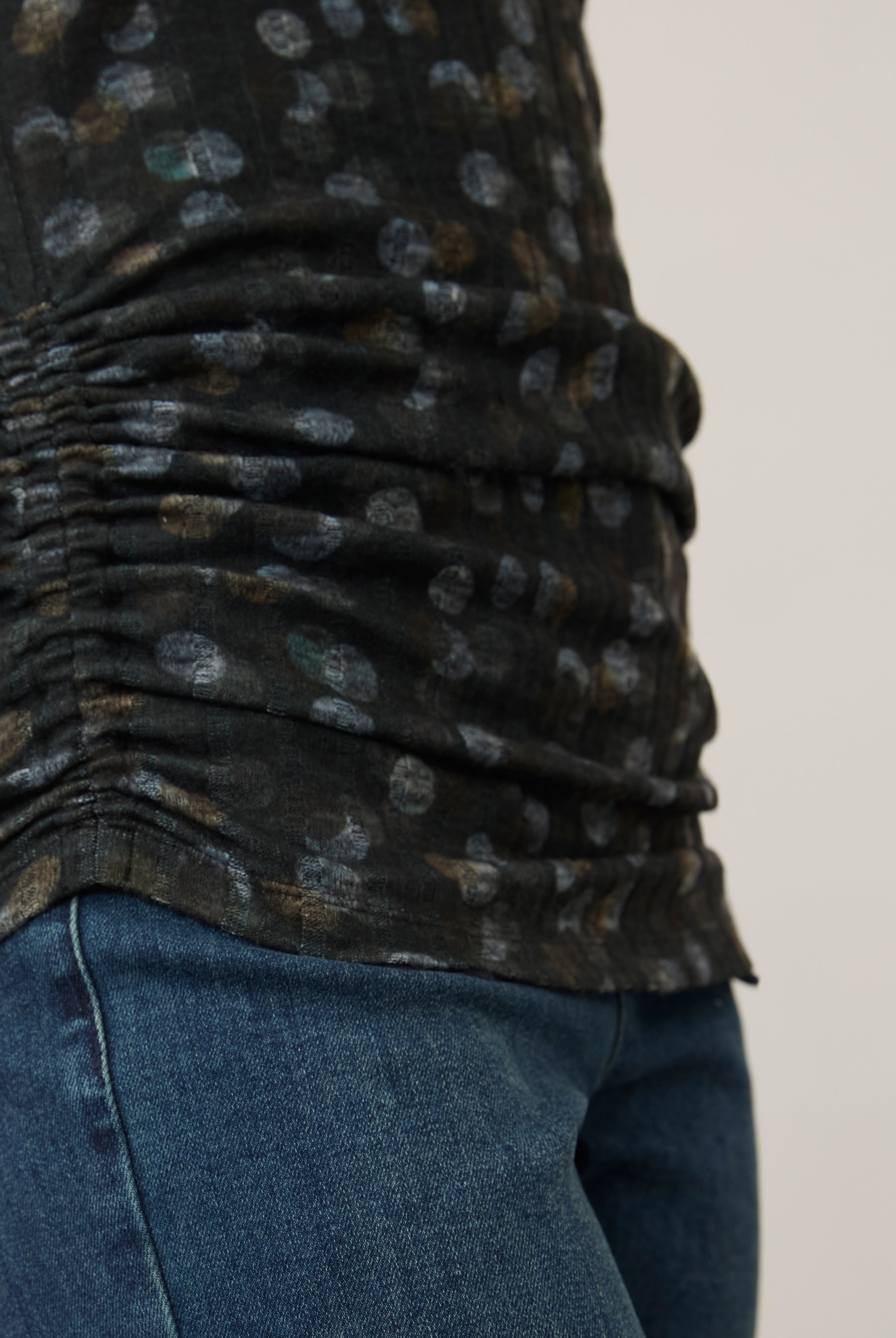 Side detail of ruched hem on black polka dot top, paired with denim jeans by French Dressing Jeans (FDJ)