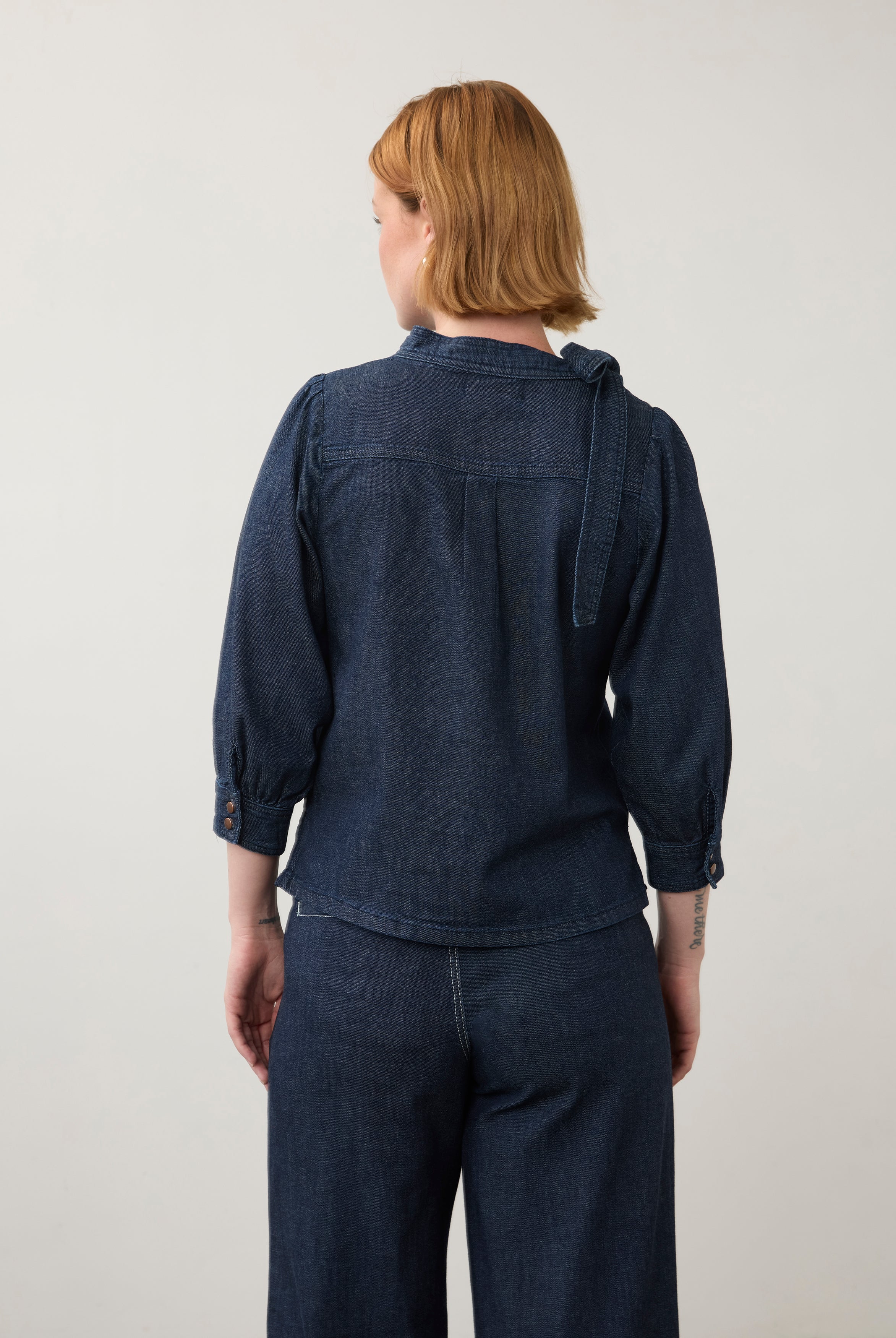 Back view of dark wash puff-sleeve top with buttoned cuffs and pleated back detail by French Dressing Jeans (FDJ)