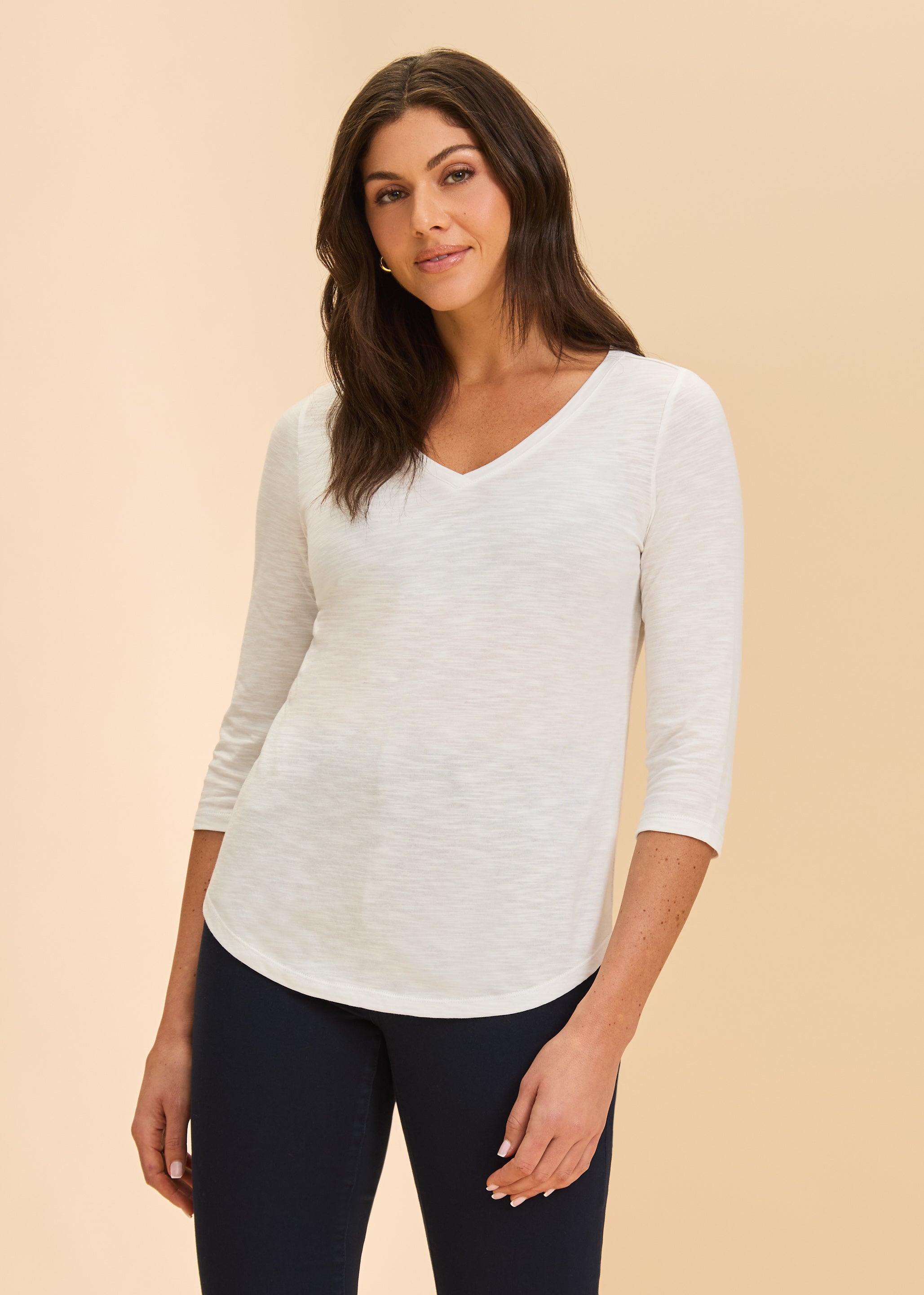 Front view of white V-neck 3/4 sleeve top with curved hem and dark pants by French Dressing Jeans (FDJ)