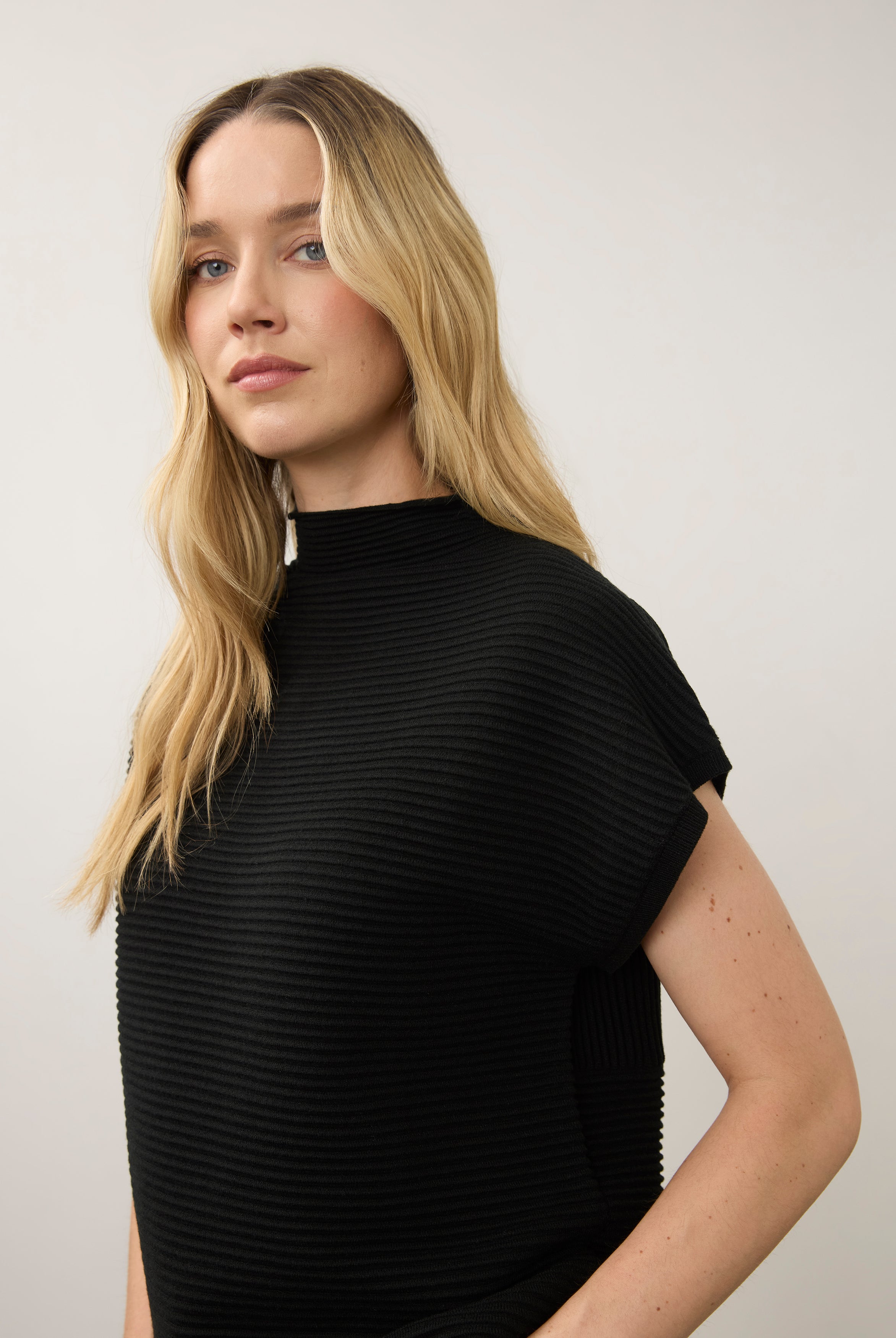 Side view of black ribbed top highlighting high collar and short sleeves by French Dressing Jeans (FDJ)