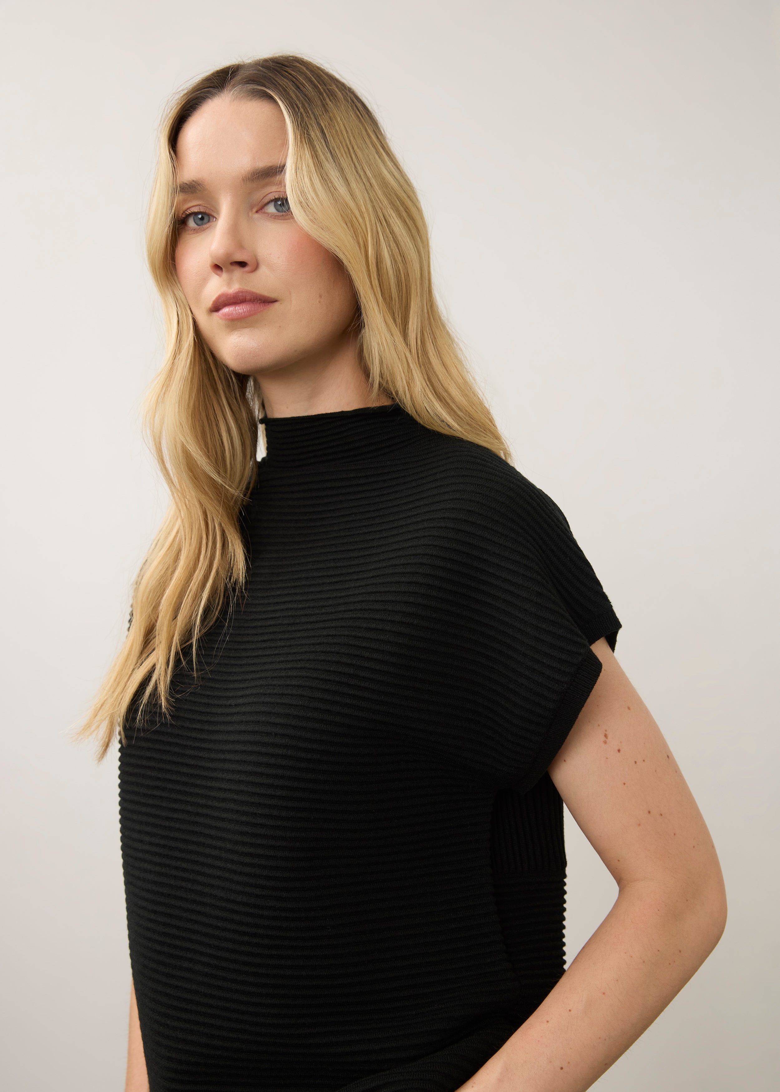 Side view of black ribbed top highlighting high collar and short sleeves by French Dressing Jeans (FDJ)