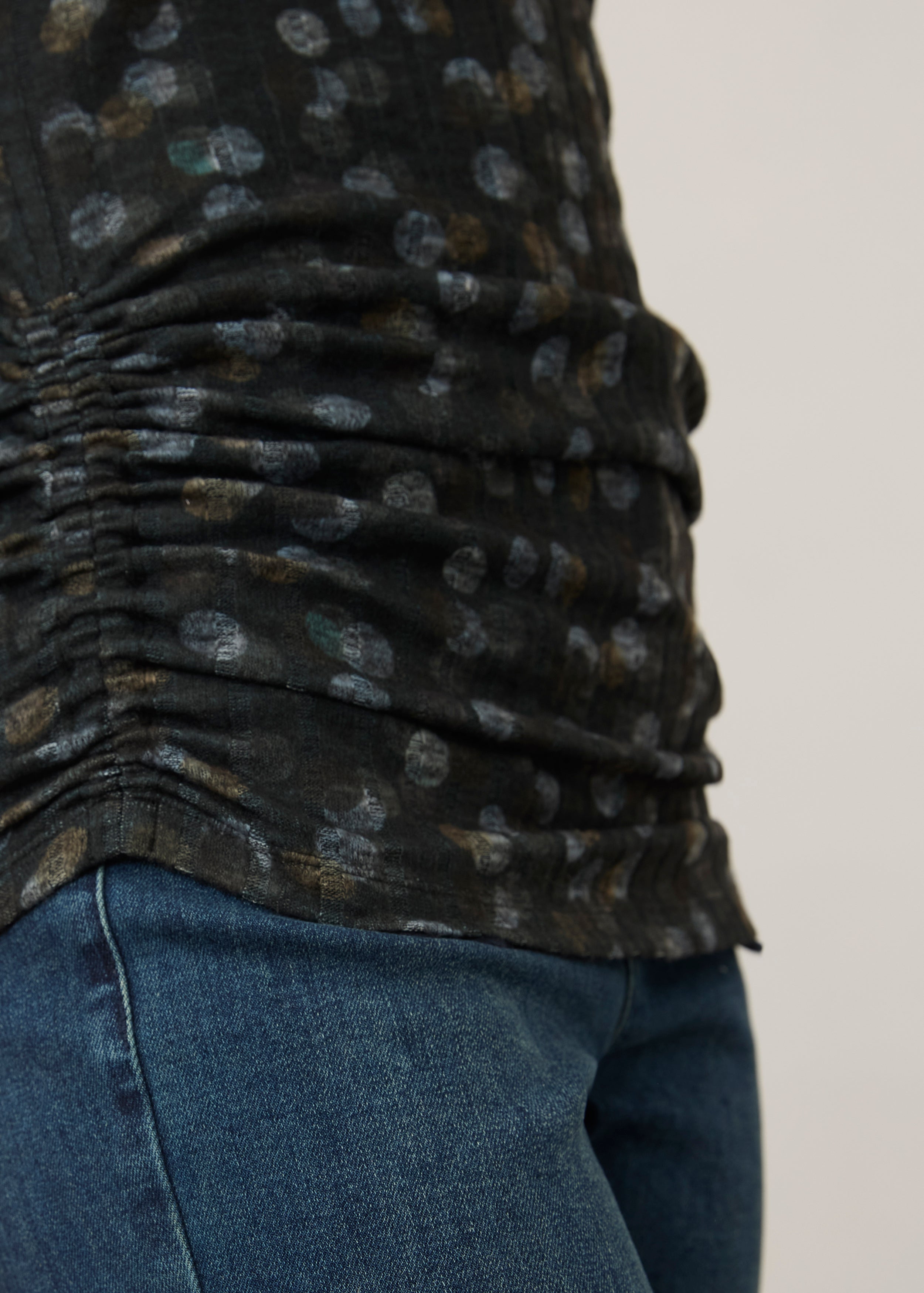 Side detail of ruched hem on black polka dot top, paired with denim jeans by French Dressing Jeans (FDJ)