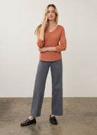 Full body view of orange V-neck top paired with gray pants for a modern look by French Dressing Jeans (FDJ)