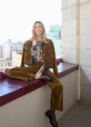 Model seated on a ledge wearing brass Olivia wide leg denim with matching jacket by French Dressing Jeans (FDJ)