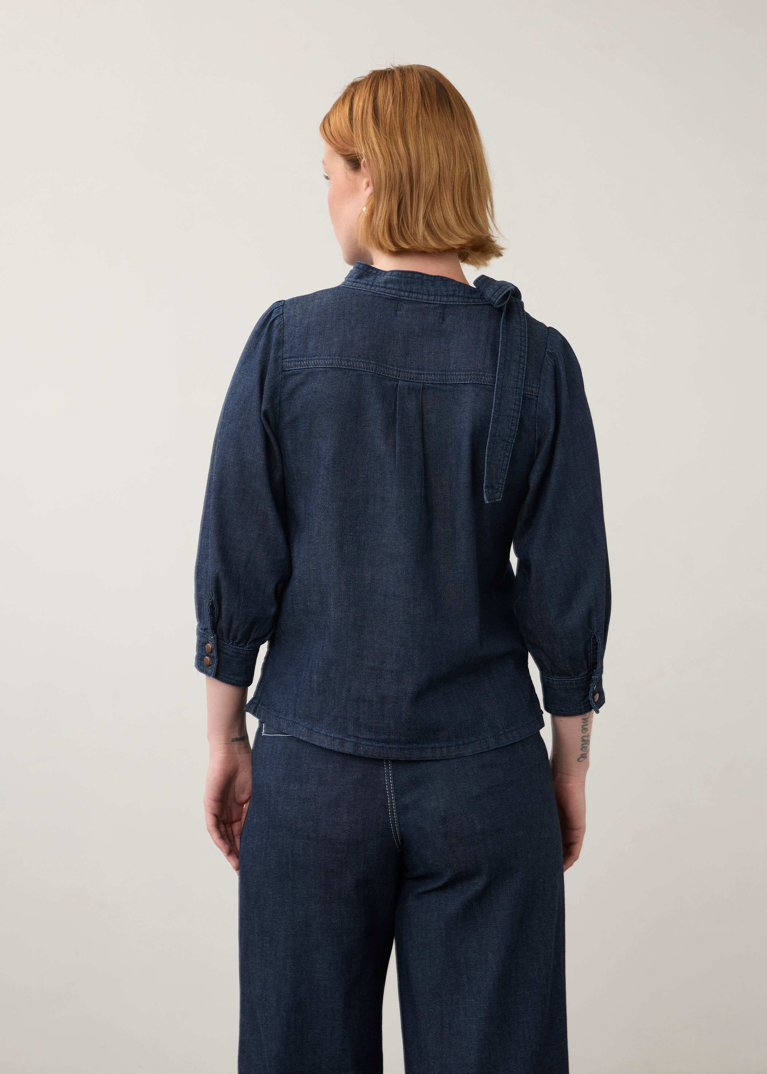 Back view of dark wash puff-sleeve top with buttoned cuffs and pleated back detail by French Dressing Jeans (FDJ)