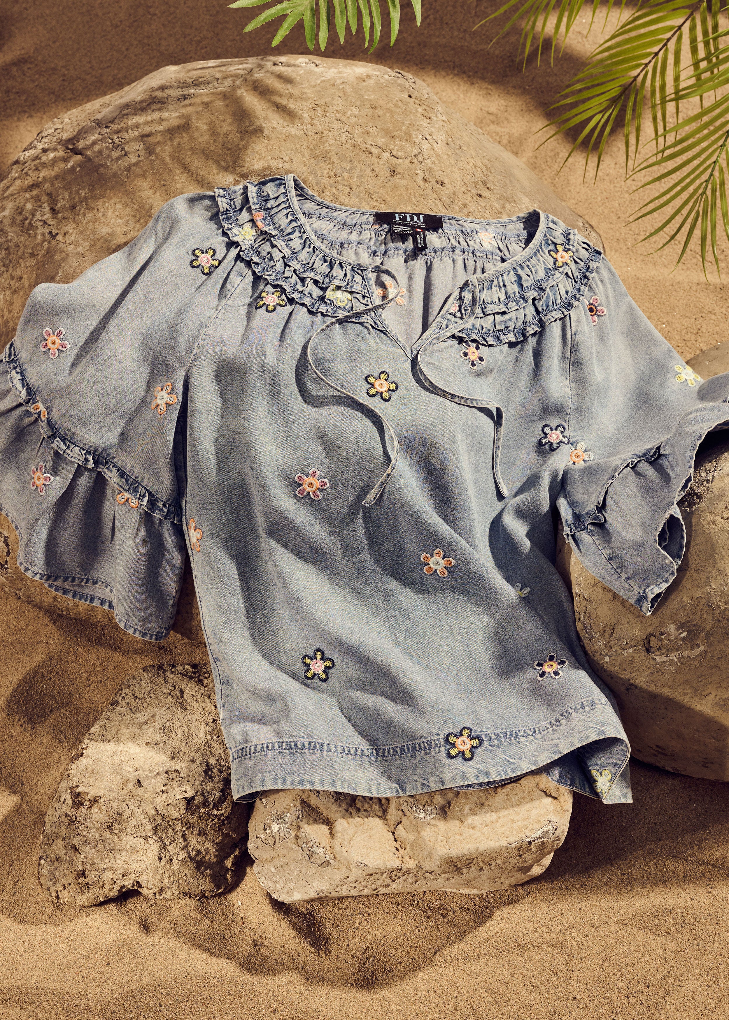 Denim top with floral embroidery and ruffled neckline on rocks by French Dressing Jeans (FDJ)