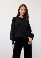 Black sweater showcasing velvet cut-out sleeve details in a standing pose by French Dressing Jeans (FDJ)